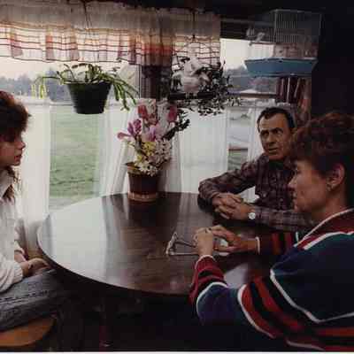 A photo view of two women and a man sitting at a table. 12/04/1989.