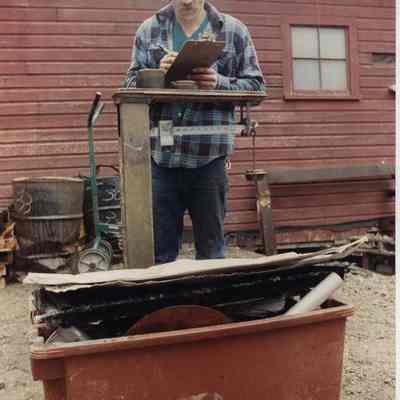 A photo view of a man weighing scrap metal. 4/20/1990.