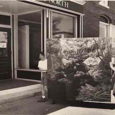 A photo view of 2 women carrying a painting. 6/2/1992.