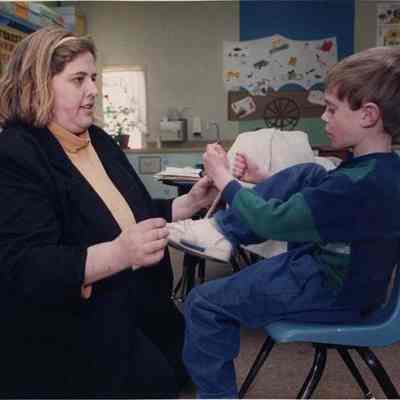A photo view of a little boy getting help tying his shoe lace. 12/10/1991.