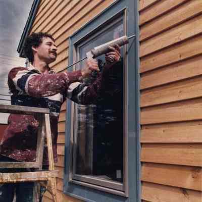 A photo view of John Sewall caulking his windows. 3/30/1989.