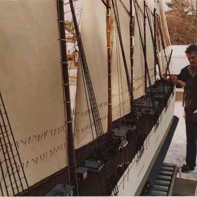 A photo view of a man adjusting a large model of a ship. 1/18/1988.