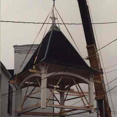 A photo view of a crane lifting a church steeple. 12/10/1990.