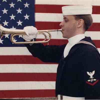 A photo view of a Navy bugler in front of an American flag. 5/21/1990.