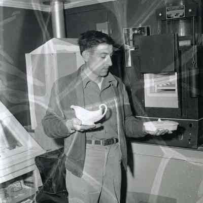 A photo of a man holding 2 dishes made from feldspar. 1955