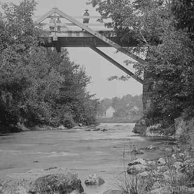 Falls Bridge on the Dennys River.: Houses and barn on the Milwaukee Road in Dennysville, seen under the Falls Bridge over the Dennys River, in a photograph taken by John P. Sheahan of Edmunds c. 1885.