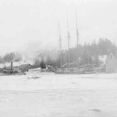Schooner Jennie French caught in the ice on the Dennys River: Peter E. Vose's wharf is seen behind the steam tug "Spray" attempting to free the icebound schooner from T.W. Allan's storehouse and loading ground to the right.  The house of Thomas Eastman, Jr. is visible on the far left.