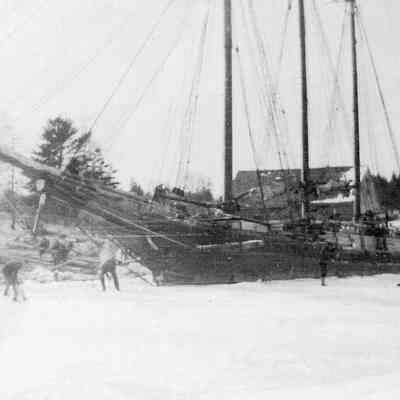 Schooner Jennie French caught in the ice at Allan's Wharf, on the Dennys River, Edmunds, Maine: Allan's warehouse is visible behind the schooner, with the Congregational Church and Lincoln House on the Dennysville side of the river are seen on the opposite side of the Dennys River.