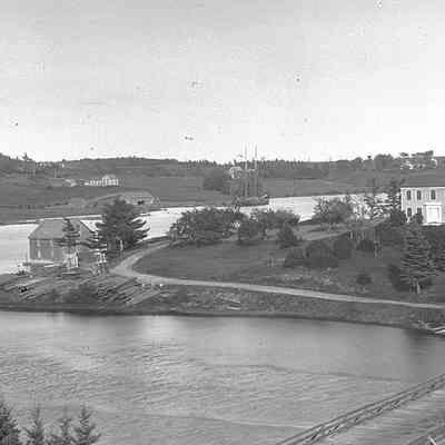 View of the Houses, Wharves and Boats on the Dennys River.: The Jones-Sheahan house is visible across the Dennys River, behind the spars of the schooner tied up by T.W. Allan's shipyard on the Narrows Road, in this photograph by John P. Sheahan of Edmunds, c. 1880.