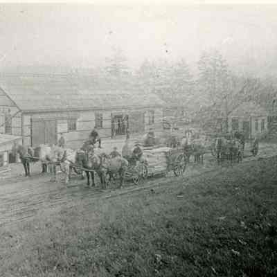 Dennysville Lumber Company, Dennysville Maine, c. 1910: Teamsters prepare to haul several heavy loads of sawn boards for the Dennysville Lumber Company.  Stacks of drying lumber were a common sight along the banks of the Dennys River during the heyday of the lumber industry.  The small square building behind the teams is the Company's office, where records were kept and the men were paid, a reminder of the economic source of the area's stability during the nineteenth and early twentieth centuries.