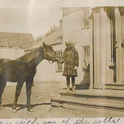 Nellie Lincoln with a colt at the Lincoln Farm in Dennysville, c. 1913.: Young Nellie Lincoln stands on the front steps of the farmhouse with one of her father's colts.  The ell, and woodshed and barn are visible in the background.