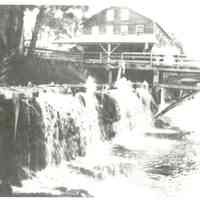          The Sluice on the Dennys River; A crowd of spectators gather on the the Upper Bridge to watch water being carried by the sluice from the mill pond to the Dennysville Lumber Company behind them. c. 1910
   
