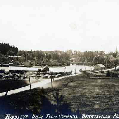 Birdseye view of Dennysville from Corn Hill, c. 1900: The site of the approach of the future U.S. Route 1 bridge over the Dennys River is covered with piles of lumber in front of the Town Wharf.   The Lower bridge is on the right, with the Congregational Church steeple rising over the tree tops beside it.