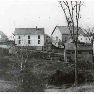 Store Hill in Dennysville c. 1897: John Allan's newly built Livery Stable dominates the skyline with T.W. Allan's Store to the left, the Riverside Inn to the right ,  and Lyman Gardner's blacksmith shop poised on the riverbank in the center.  The gable end of E.C. Wilder's old hotel, acquired by John Allan in 1865, can be seen across The Lane from the large barn.