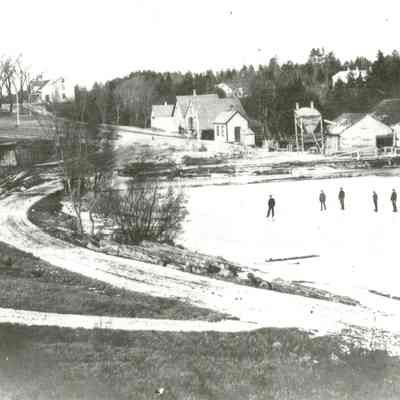 Skaters on the Dennys River Mill Pond.: Image of the Lincoln's frozen mill pond, with the mills , before 1907.  The two large buildings on the river were sold to the Dennysville Lumber Company in 1894, while the smaller buildings to the left housed the box and novelty mill, and a grist mill, both of which burned and were replaced in September of 1907.