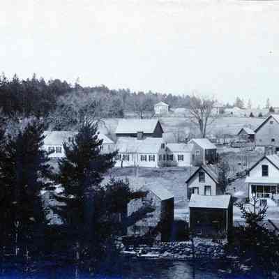 Stores and dwellings on the Dennys River with Mill Houses in the distance.: Two of three square mill houses built by the S.D. Warren Company in the early twentieth century line the horizon above the stores and houses along the Dennys River in Dennysville, Maine.