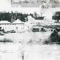         View of Dennysville Lumber Company Boarding house and mill buildings on the Edmunds side of the Dennys River; Stacks of drying lumber and saw logs surround the boarding house and other buildings belonging to the Dennysville Lumber Company on the Edmunds side of the Dennys River.  The Lyons Hills school, Stephen Lyons' and Noah Sylvia houses are visible on the hill behind.
   