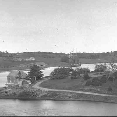 T.W. Allan's shipyard viewed across the Dennys River from Dennysville.: T.W. Allan and Son's shipyard can be seen on the far bank of the Dennys River below Foster's Lane.  A long barn, wharf and tall masted schooner sit together on the tidewater of the river in this photograph by Dr. John P, Sheahan, taken around 1880.